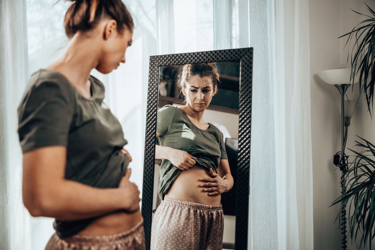 body image issues, a women looking at her stomach in the mirror