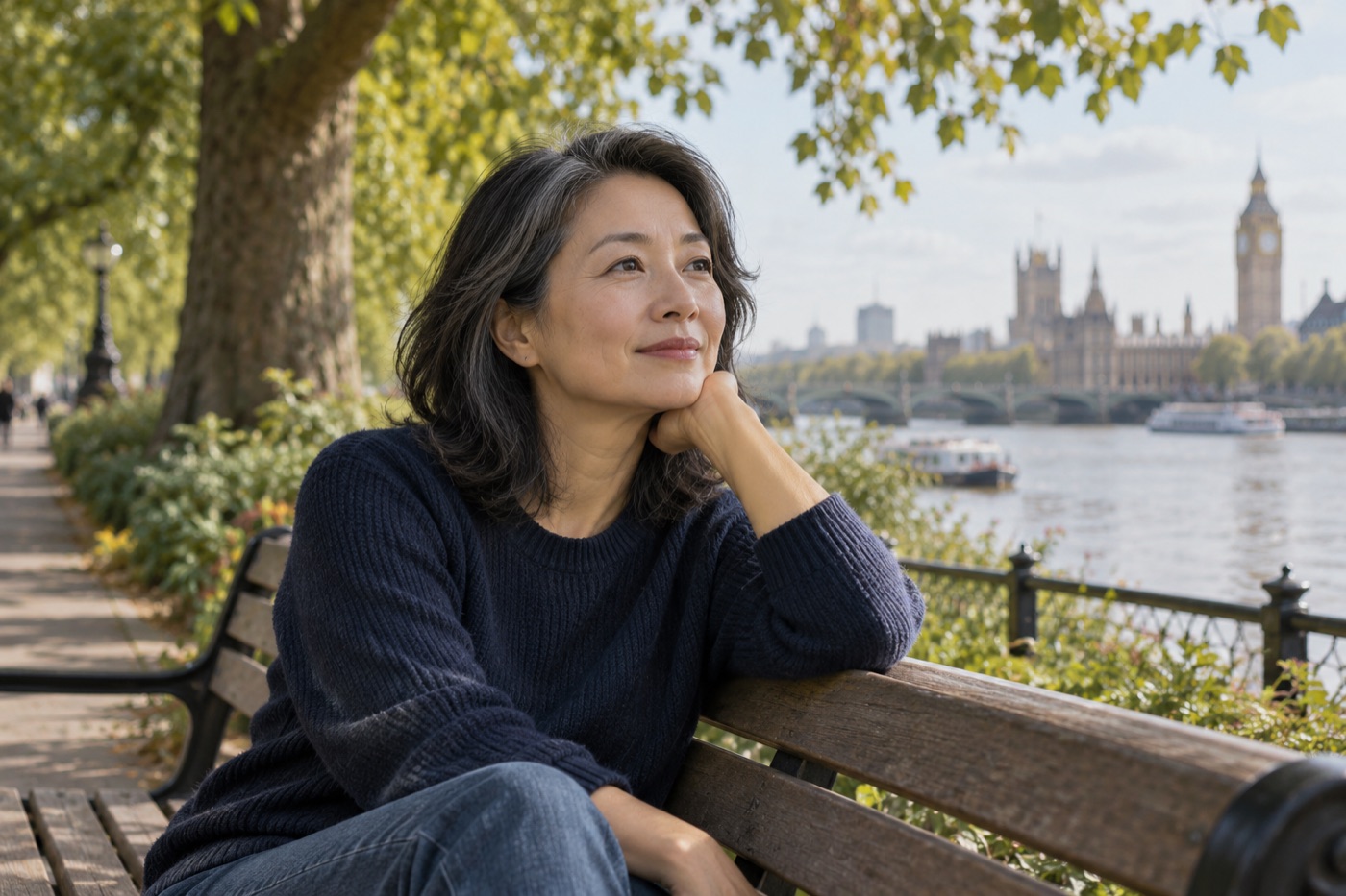 Woman sitting on a wooden bench beside trees overlooking the River Thames