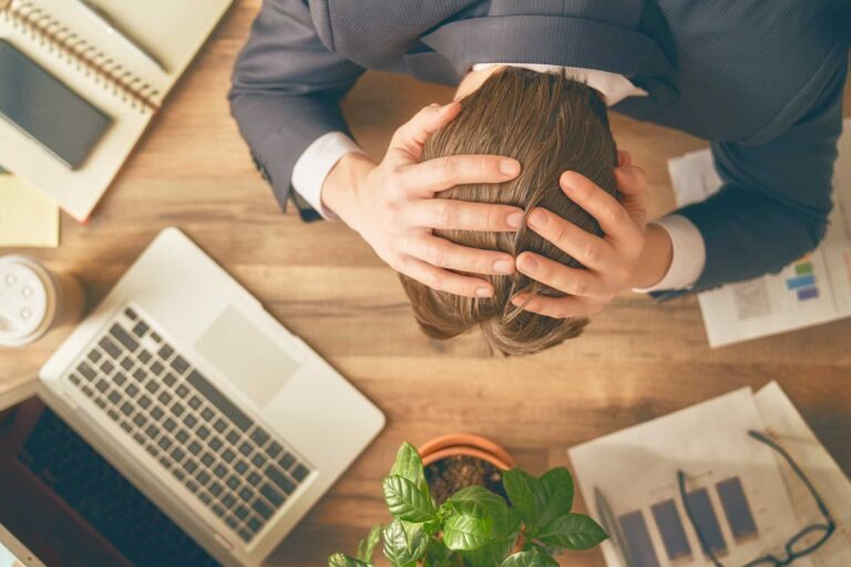 ocd stress management, A stressed worker with hands on his head over a work desk.