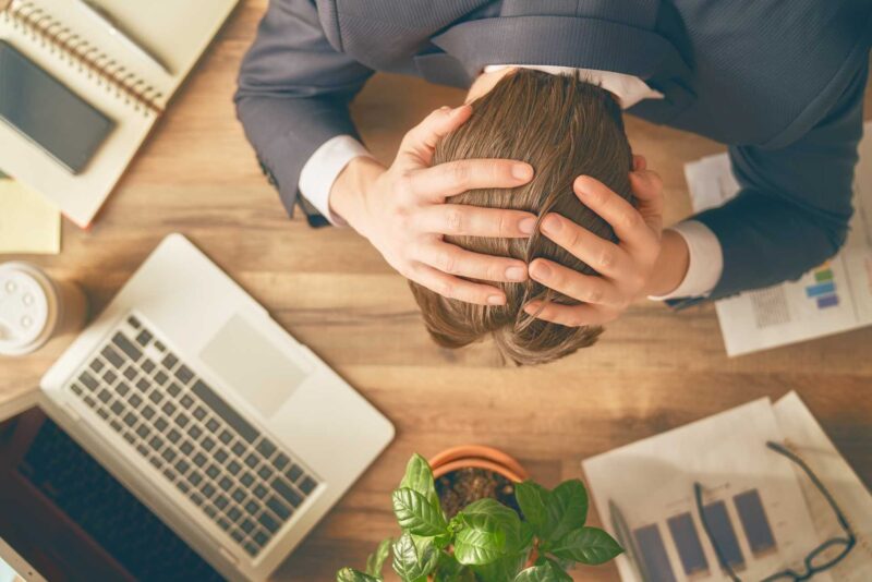 ocd stress management, A stressed worker with hands on his head over a work desk.