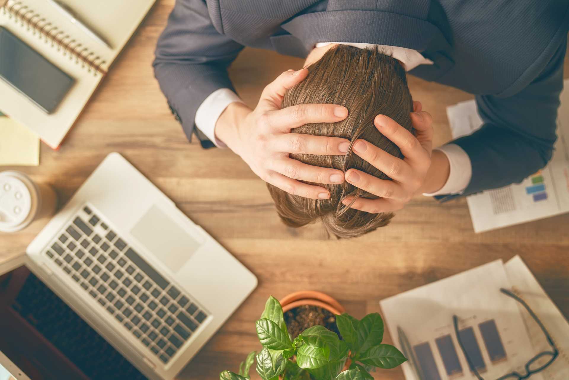 ocd stress management, A stressed worker with hands on his head over a work desk.