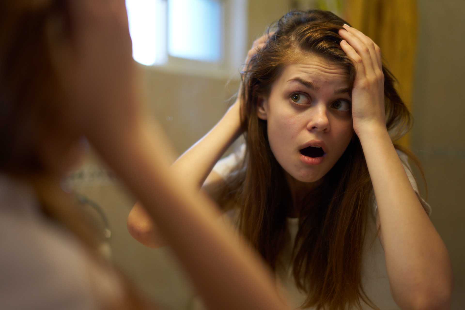 stop pulling hair, a woman expresses concern, looking at her hair in the mirror.